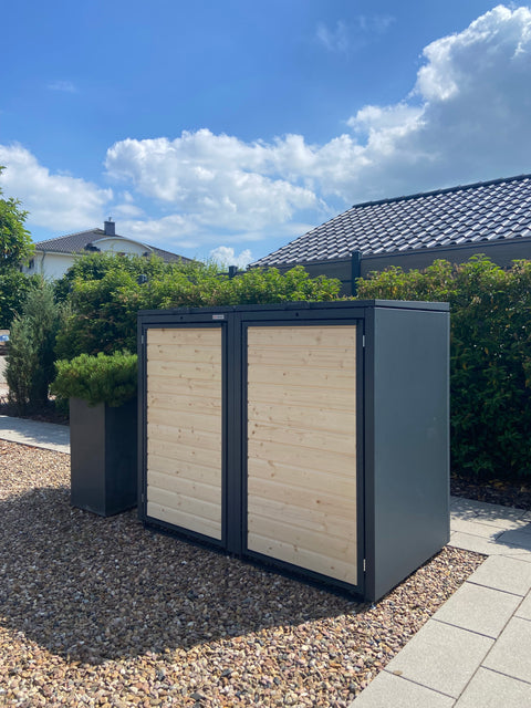 Two BIO Stefan trash bin boxes in modern design stand on a gravel path under a cloudy sky.