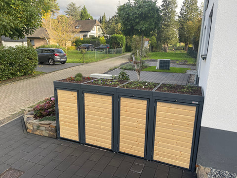 A BIO Stefan trash bin box with a planted roof stands decoratively next to a residential house.