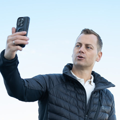 A person in a black jacket is holding a smartphone up in the air.