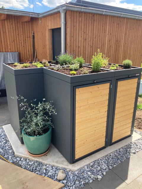 BIO Stefan garbage bin box with green roof and wooden cladding in a garden.