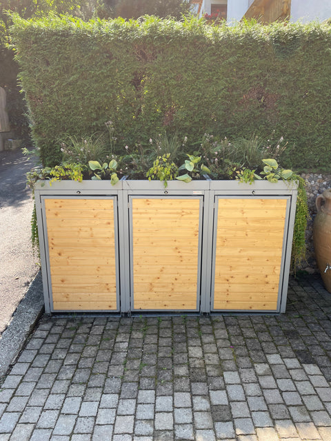 Trash bin box made of wood and metal with a green roof by BIO Stefan in front of a green hedge.