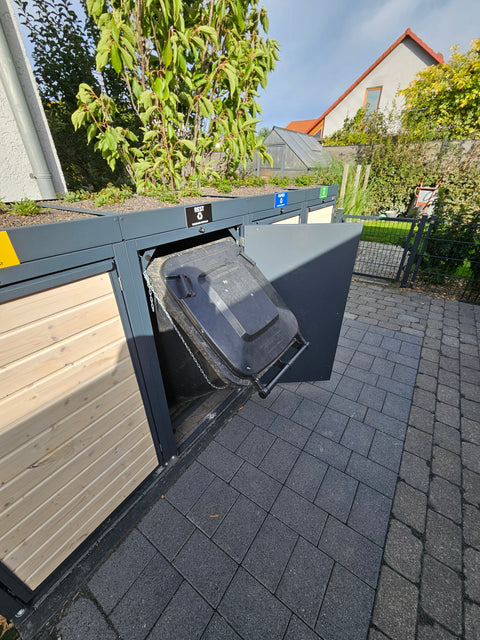 Wooden garbage bin box from Bio Stefan with an open residual waste bin in front of a garden.