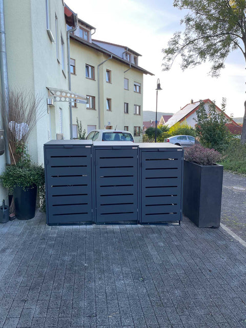 BIO Stefan Alubert Mülltonnenbox 3er 240l in Anthrazit freistehend auf gepflasterter Hofeinfahrt zwischen Pflanzkübeln