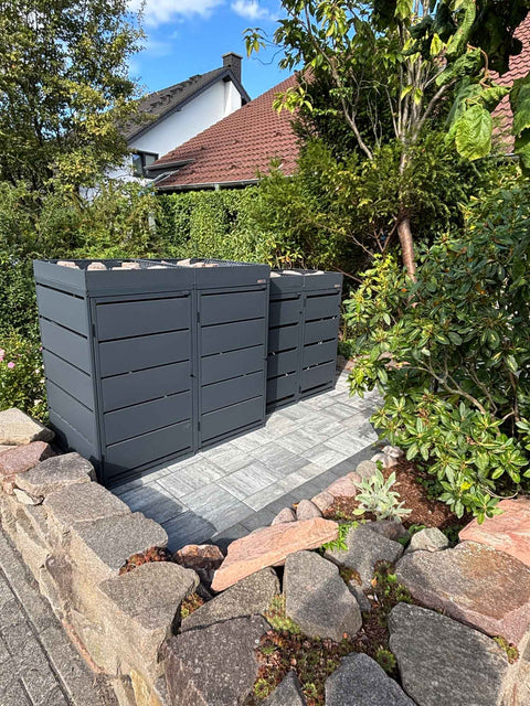 BIO Stefan Dagobert Mülltonnenbox 4er Kombination 120l und 240l in Anthrazit mit Pflanzdach, seitlich neben Natursteinmauer und Rhododendron