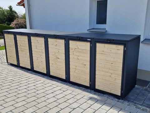 BIO Stefan Holzmichl Mülltonnenbox 6er 240l in Anthrazit RAL 7016 mit naturbelassener Fichtenholzfront, seitliche Ansicht an der Hausfassade auf gepflasterter Einfahrt