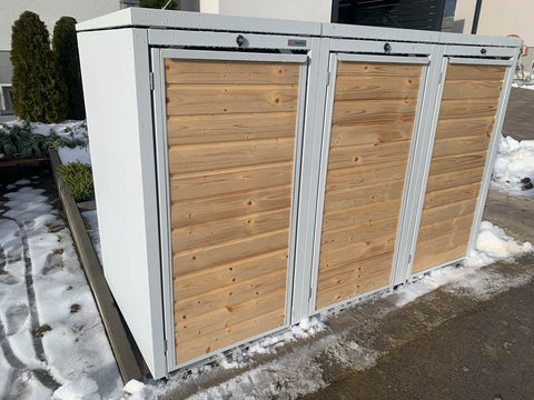 BIO Stefan Holzmichl Mülltonnenbox 3er 120l in Reinweiß RAL 9010 mit Fichtenholz-Front auf gepflastertem Streifen neben Hochbeet und Hecke im Winter