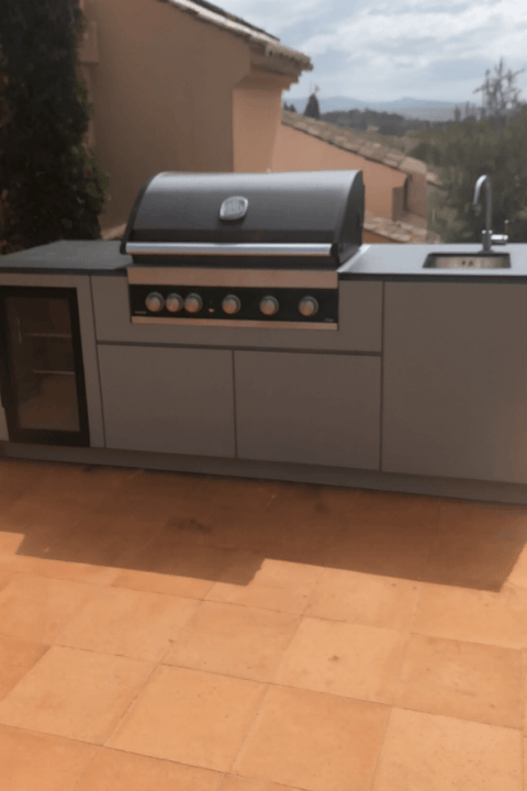 Modern outdoor kitchen with grill and sink on a terrace.
