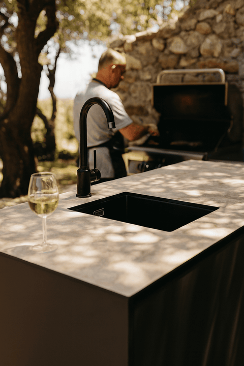 Modern outdoor kitchen with stone countertop and faucet, grill area in the background.