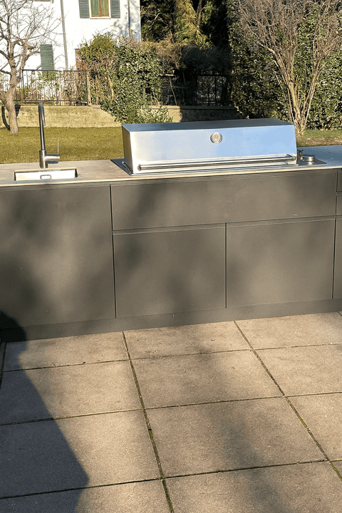 Modern outdoor kitchen with sink and grill against a garden backdrop.