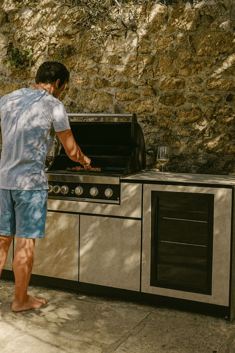 Man grills at a BIO Stefan outdoor kitchen in front of a stone wall.
