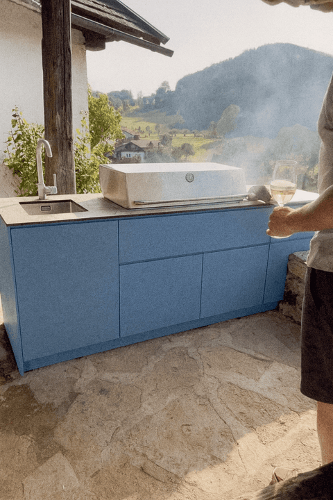 Blue outdoor kitchen with grill and sink against a landscape background.