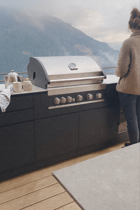 Outdoor kitchen with grill and mountain view, person standing next to it.