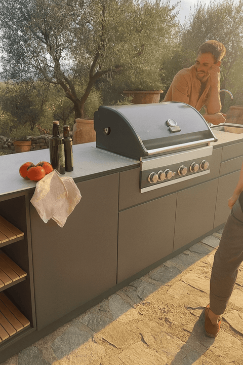 Outdoor kitchen with grill and bottles, a man leans on it smiling.