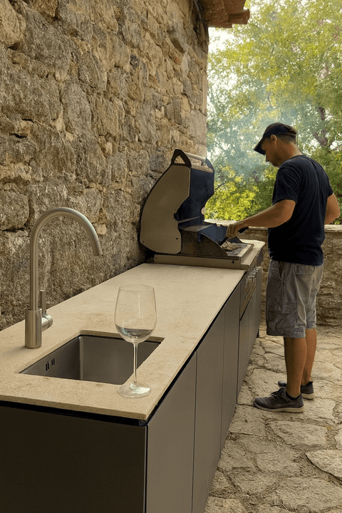 Outdoor kitchen made of stone with grill and glass on the countertop.
