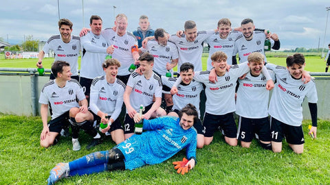 Soccer team wearing BIO-STEFAN jerseys celebrates laughing and poses on the field.